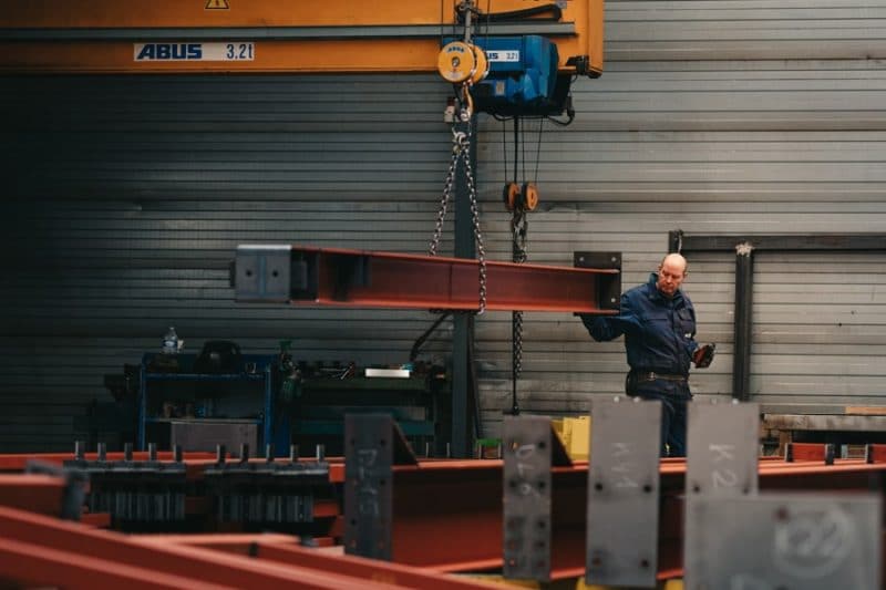 Een medewerker van edibo is bezig met een project in de industriebouw. Hij is bezig met stalen poutrel te verplaatsen binnen een magazijn of werkruimte.