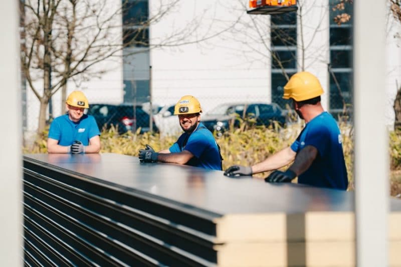 Medewerkers van edibo pauzeren tijdens een industriebouw-project. Ze staan buiten, hebben blauwe T-shirts aan en dragen een gele helm.