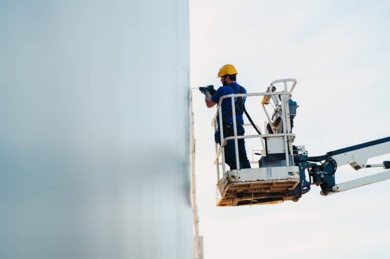 Een edibo-medewerker is aan het werk op een hoogtewerker, aan een industriebouw.