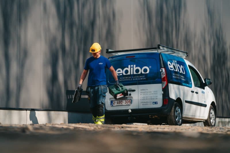 Een medewerker van edibo wandelt langs zijn bestelwagen, die volledig bestickerd is. De kleuren zijn blauw en wit.