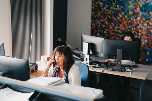 Een collega van de ondersteunende diensten van edibo zit achter haar bureau, en is aan het telefoneren met een klant over hun industriebouw.