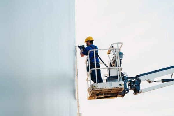 Een edibo-medewerker is aan het werk op een hoogtewerker, aan een industriebouw.