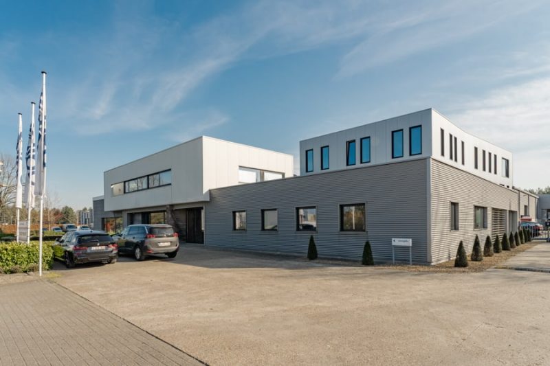 De buitenkant van het kantoor van edibo, specialist in industriebouw. Het is een moderne bouw met een grijze gelijkvloersverdieping en wit eerste verdieping.