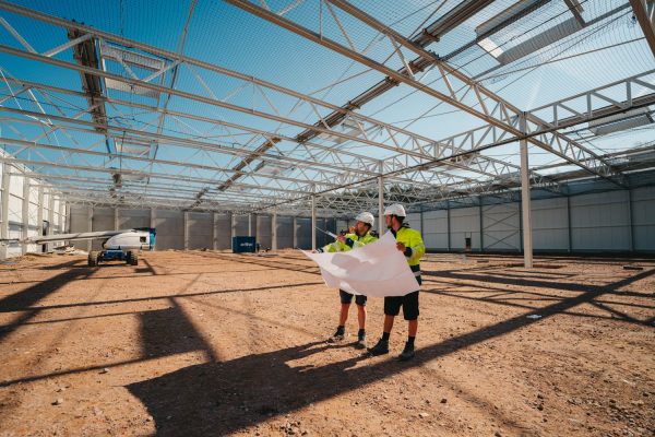 Twee collega's van edibo staan op een grote werf van een industriebouw. Ze hebben een groot plan in hun handen dat ze samen bespreken.